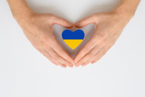 immagine di due mani che si chiudono a cuore su una bandiera ucraina